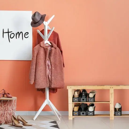 Zwarte Relaxdays schoenenorganizers met schoenen onder een houten bankje in een hal met oranje muur, witte kapstok en roze jas