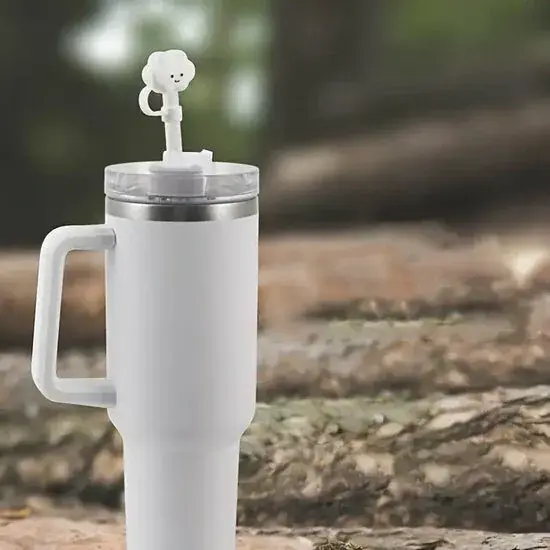 Wit rietjesdopje in de vorm van een wolkje met gezichtje op het rietje van een witte thermosbeker met handvat, buiten tussen boomstammen